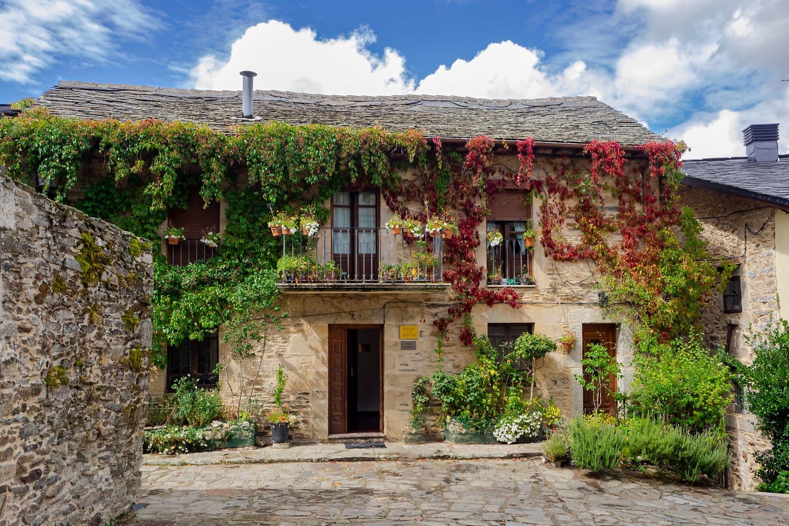 Casa tradicional de piedra con balcón de madera y fachada cubierta de hiedra