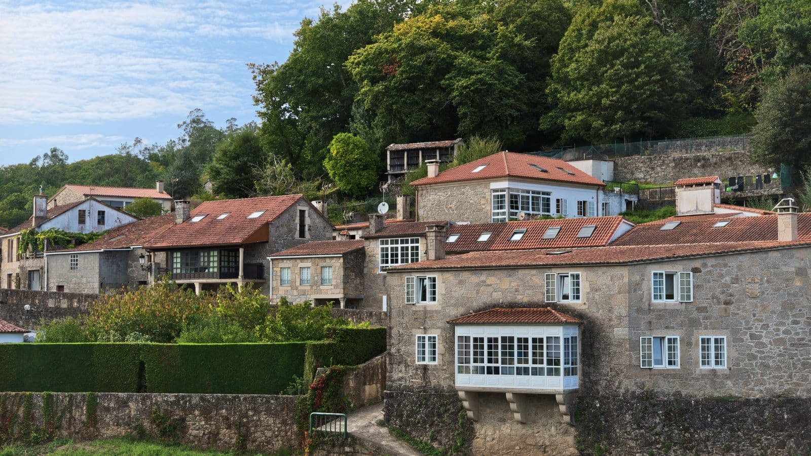 Casas de piedra con tejados de teja entre árboles, una de ellas con galería acristalada blanca