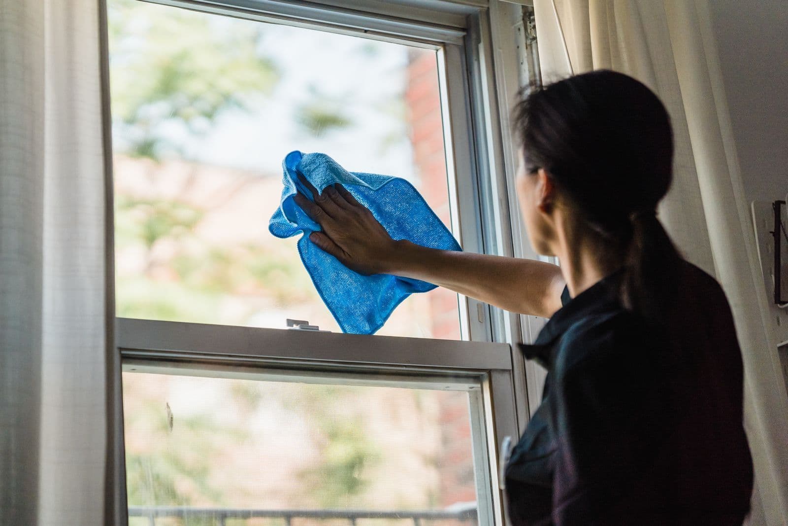 Mujer limpiando con un paño el cristal de una ventana de guillotina desde dentro