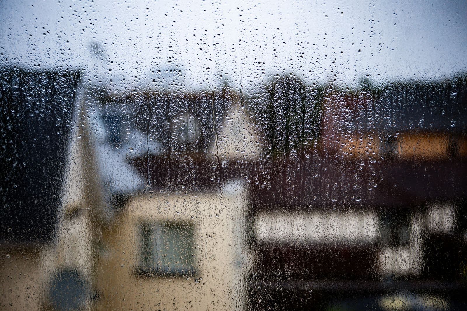 Gotas de lluvia sobre el cristal de una ventana con tejados desenfocados al fondo