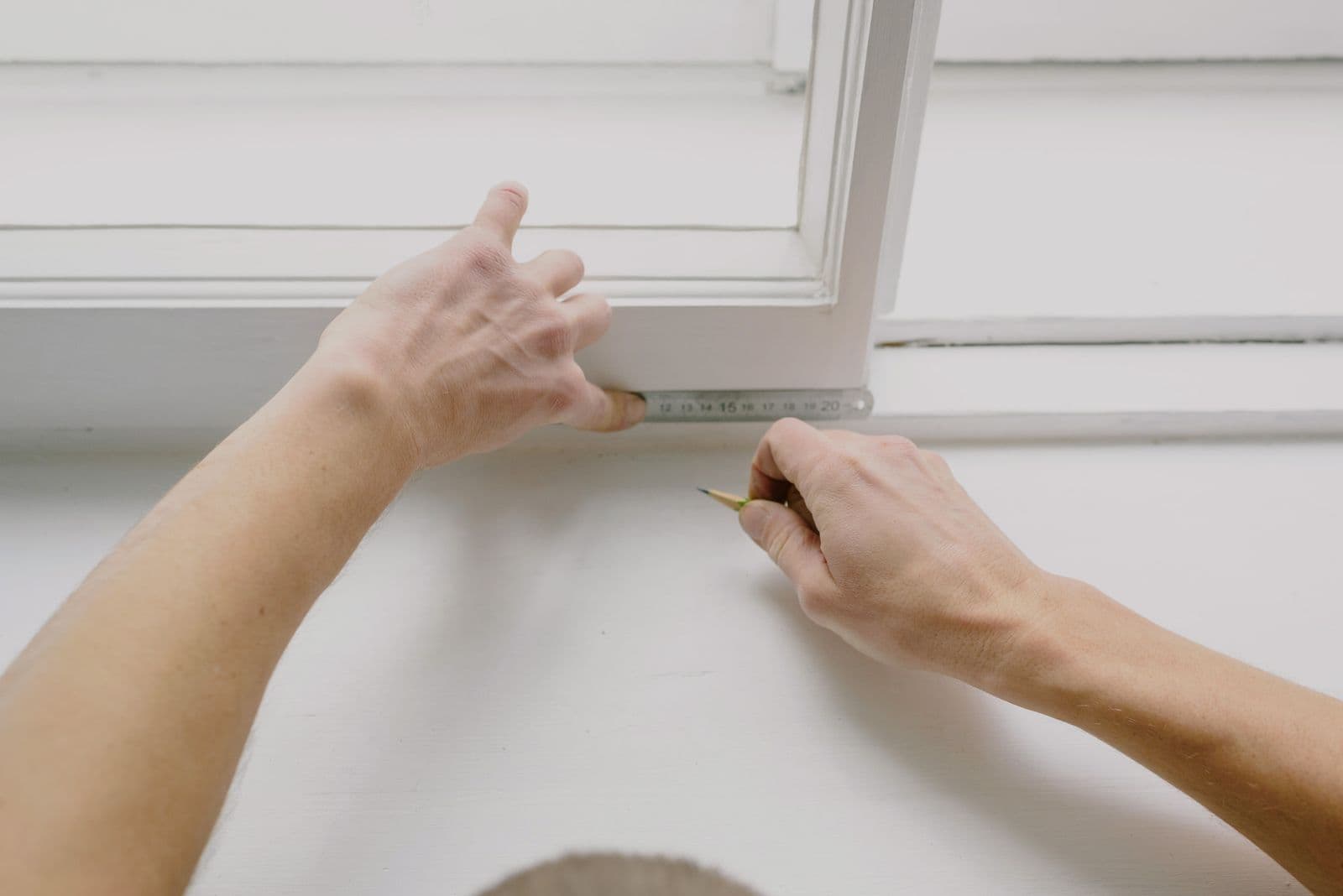 Manos midiendo con un flexómetro el marco de una ventana blanca y marcando con lápiz