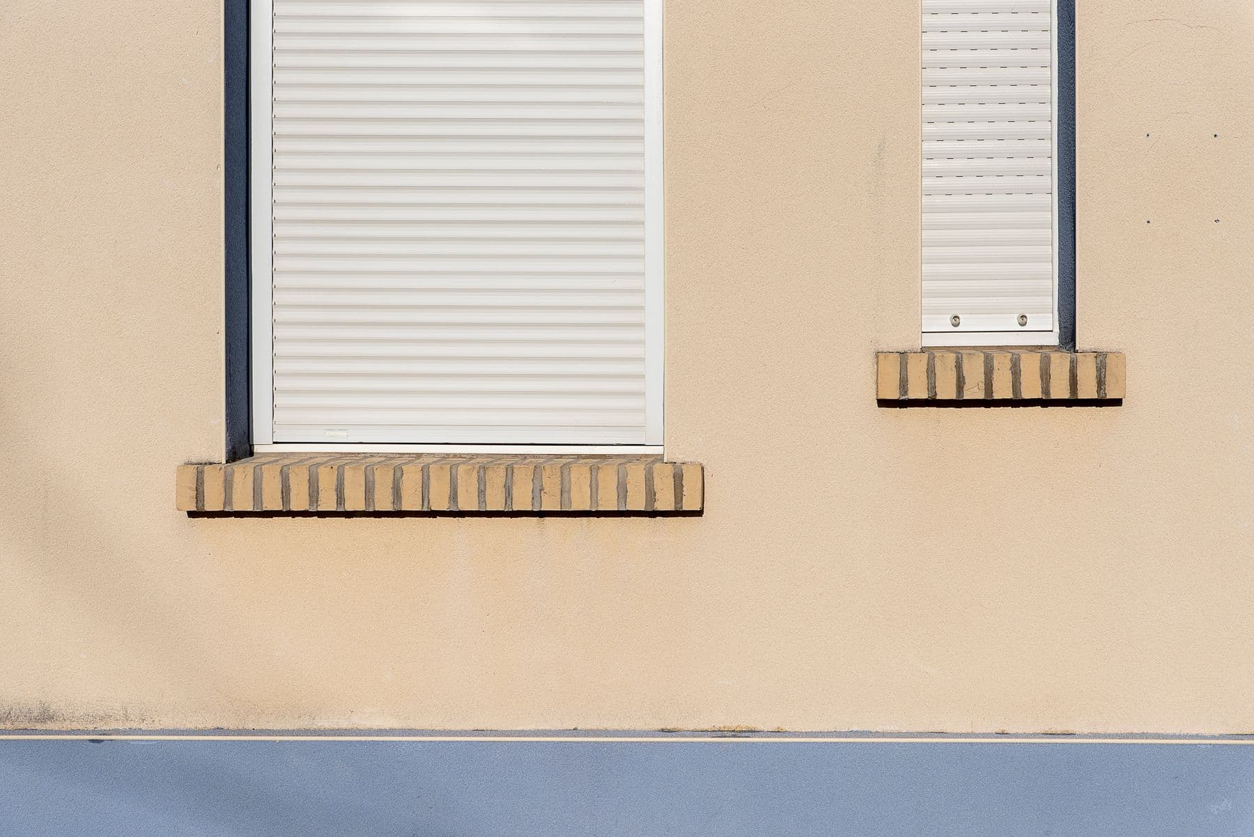 Fachada clara con dos ventanas y sus persianas enrollables blancas bajadas