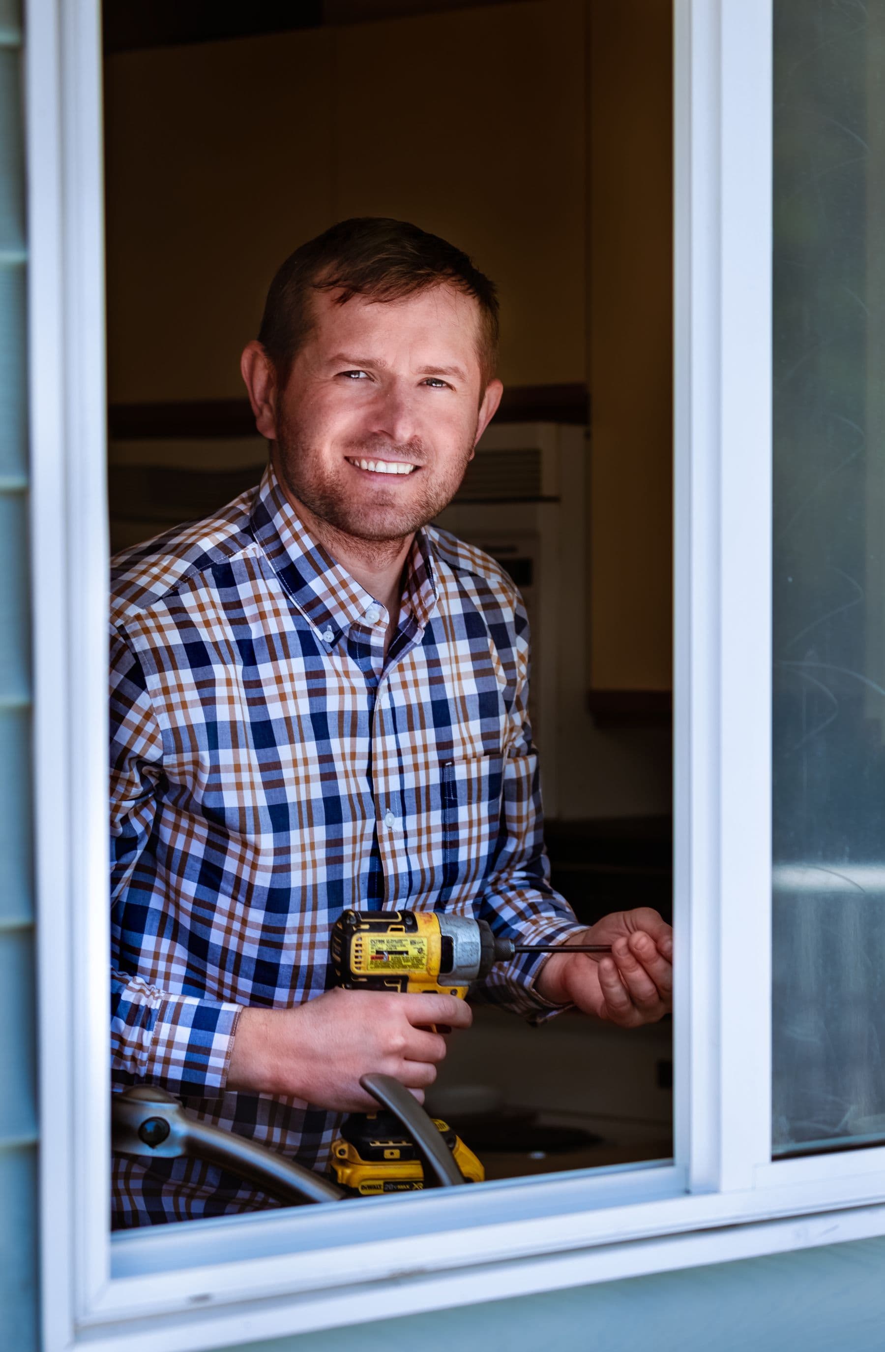 Técnico sonriente con un taladro, visto a través de una ventana abierta