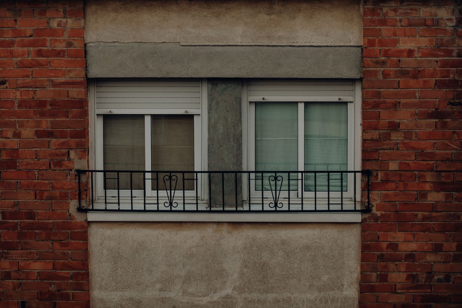 Ventana doble con balconcillo de forja y cajón de persiana sobre una fachada de ladrillo